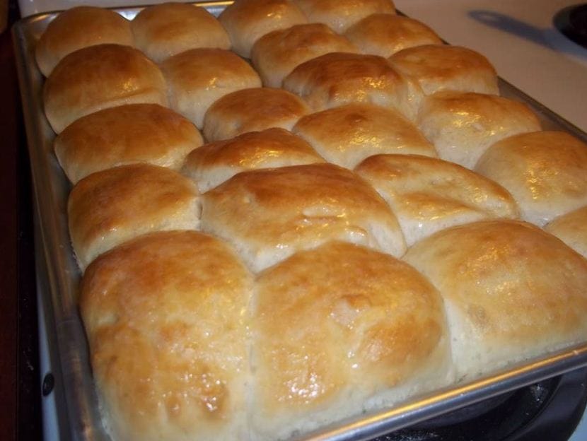 A close-up photo of a plate piled high with warm, golden brown Texas Roadhouse rolls, ready to be devoured.