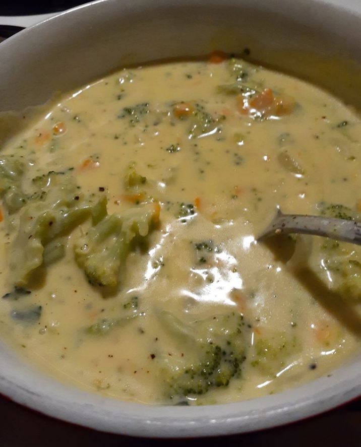 Slow Cooker Broccoli Cheese Soup in a white bowl, topped with shredded cheddar and parmesan cheese.