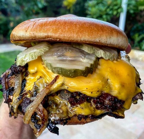 A photo of a juicy burger topped with crispy fried onions, served on a bun.