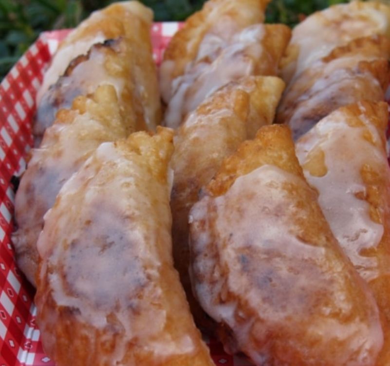 Homemade fried apple pies on a plate, sprinkled with cinnamon sugar.