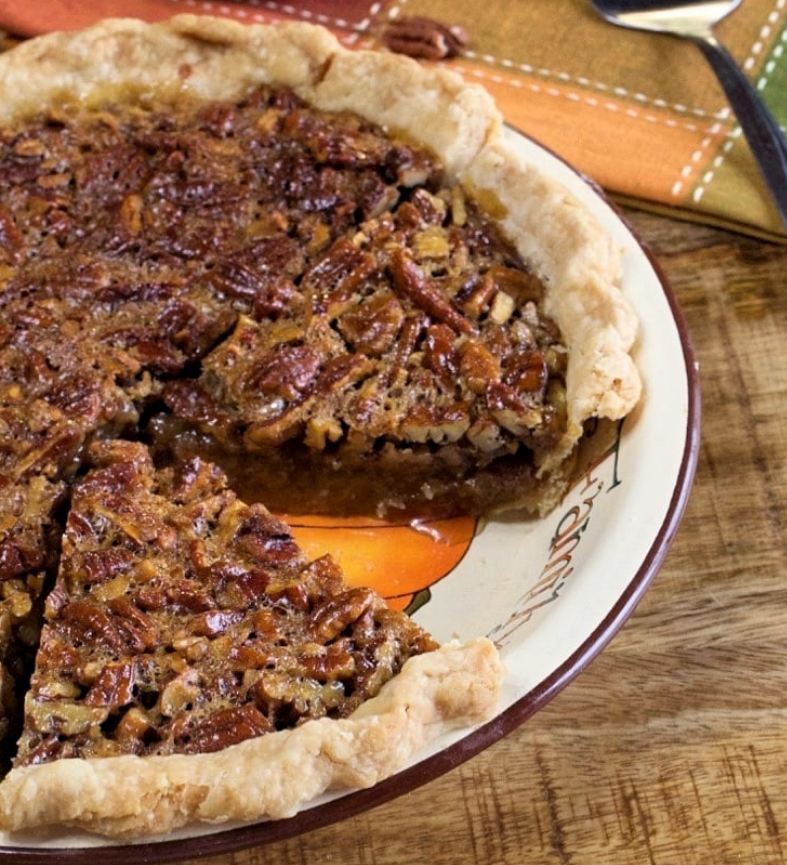 A golden brown Southern Pecan Pie on a white plate with a slice cut out.