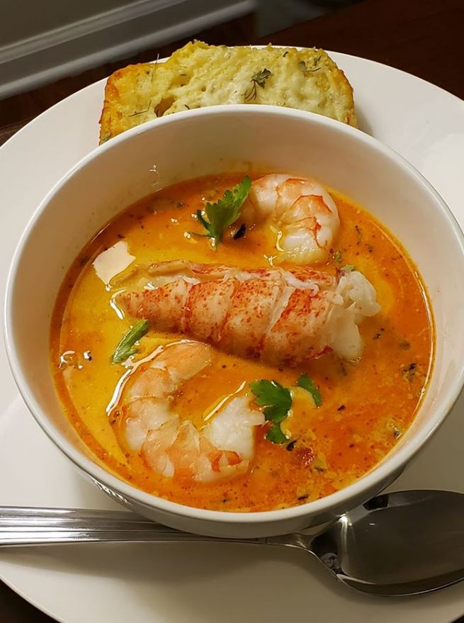Seafood Bisque with crab, shrimp, and lobster in a white bowl, served with a side of Garlic Ciabatta bread.