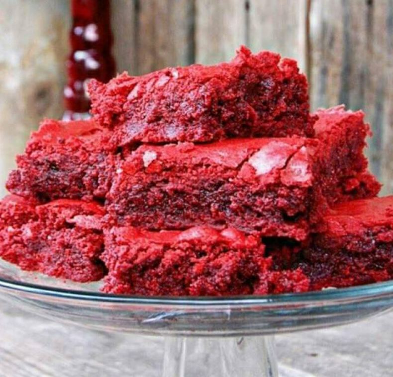 A plate of freshly baked red velvet brownies, with a creamy frosting on top