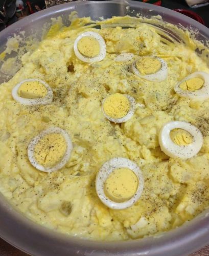 A bowl of potato salad with chopped potatoes, eggs, onions, celery, and pickles, coated in a creamy dressing.