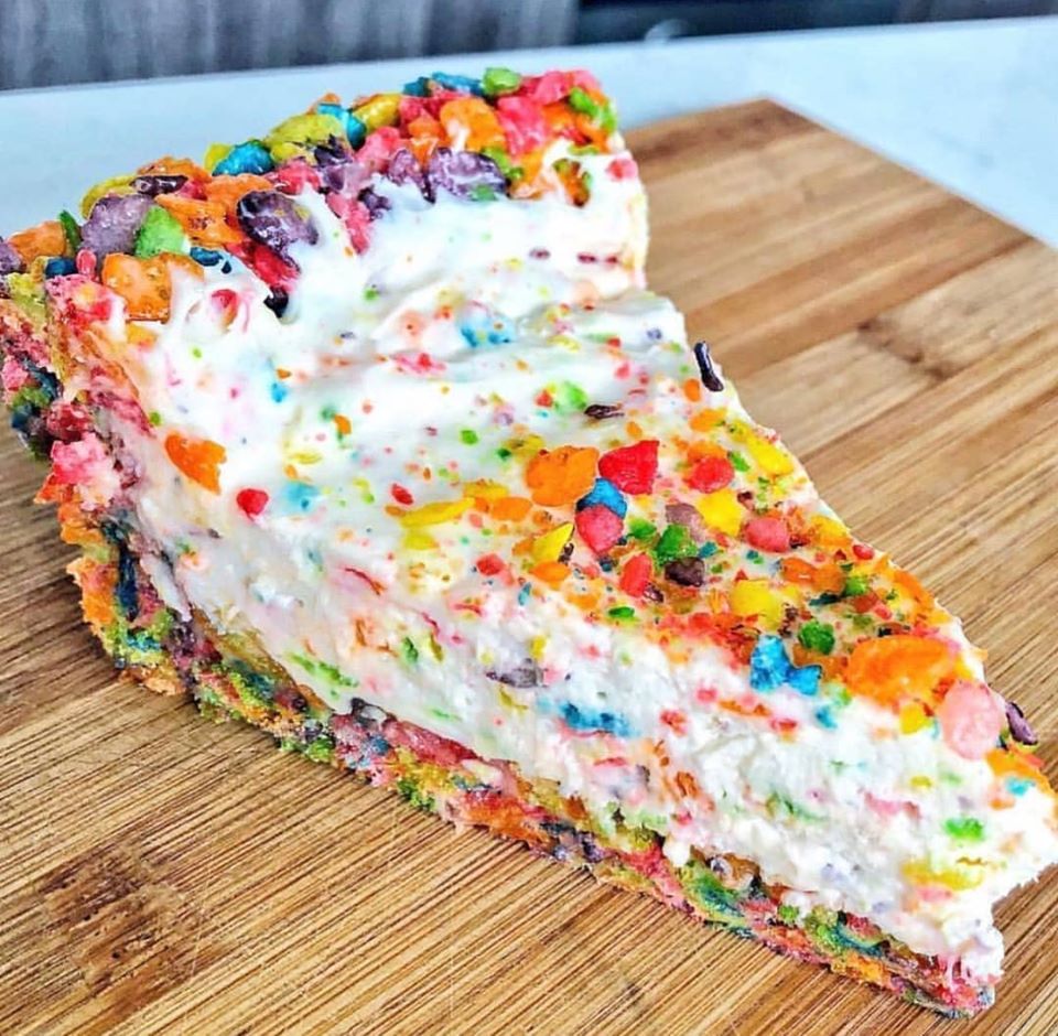 Fruity Pebbles Cheesecake on a white plate with whipped cream and Fruity Pebbles cereal on top.