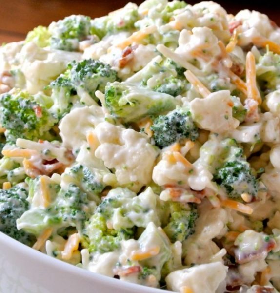 A bowl of loaded broccoli cauliflower salad with bacon, cheese, and dressing on top.