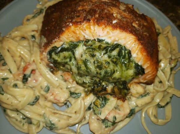 A plate of blackened salmon stuffed with spinach and parmesan cheese, with shrimp and spinach alfredo sauce on the side