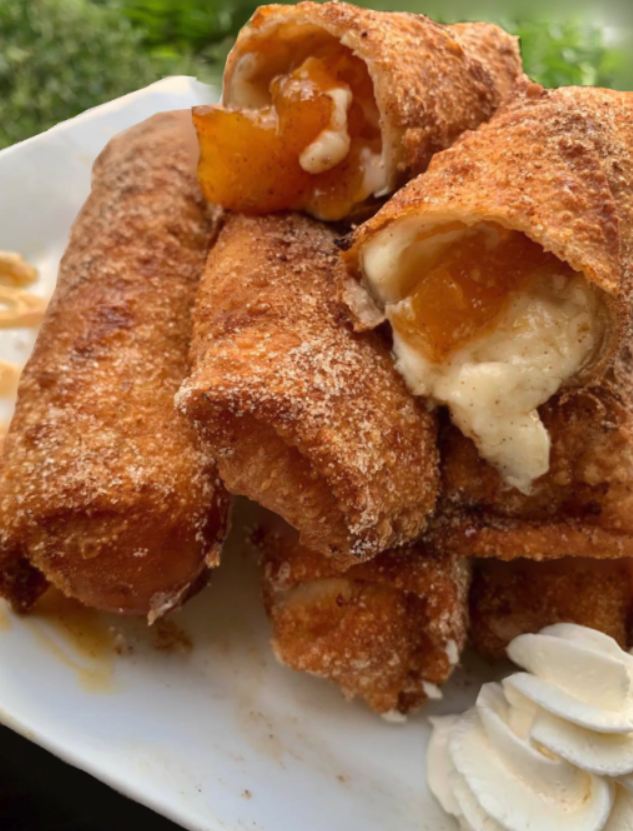 A plate of golden brown Peach Cobbler Cheesecake Stuffed Eggrolls, served with a scoop of vanilla ice cream