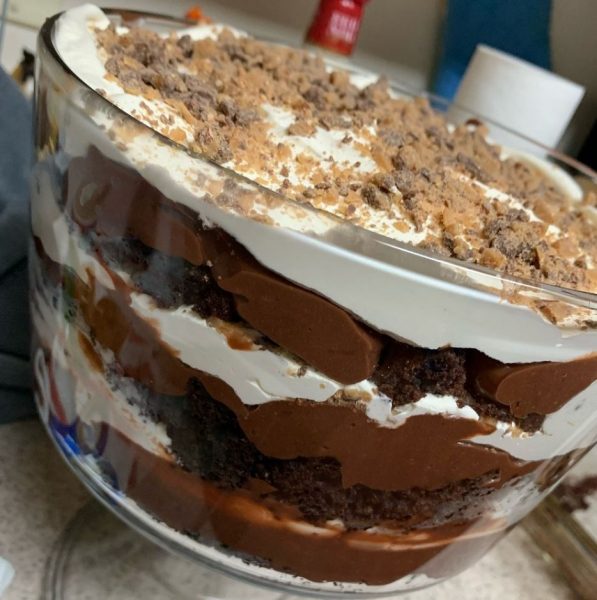 A beautiful glass trifle dish filled with layers of chocolate cake, chocolate pudding, cherry pie filling, and whipped topping.