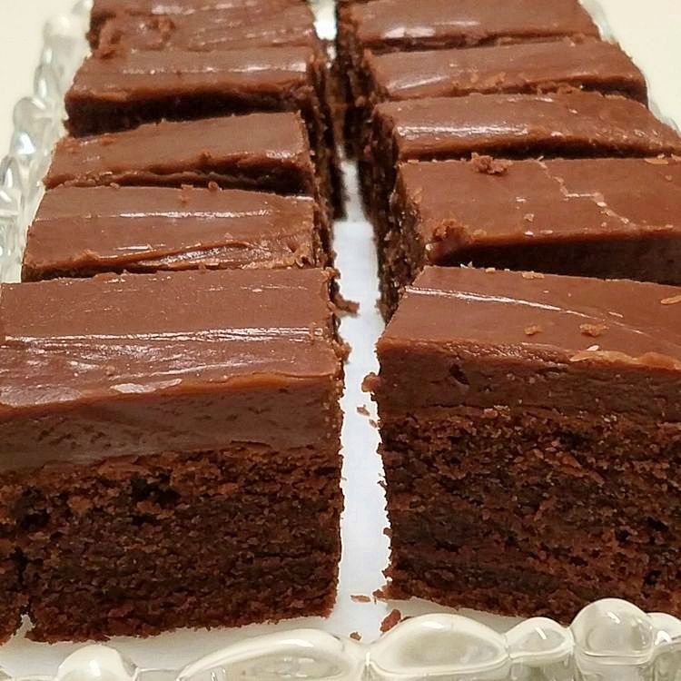 Close-up photo of warm, freshly baked chocolate fudge brownies with rich, crackly tops and gooey centers, cut into squares on a serving plate.