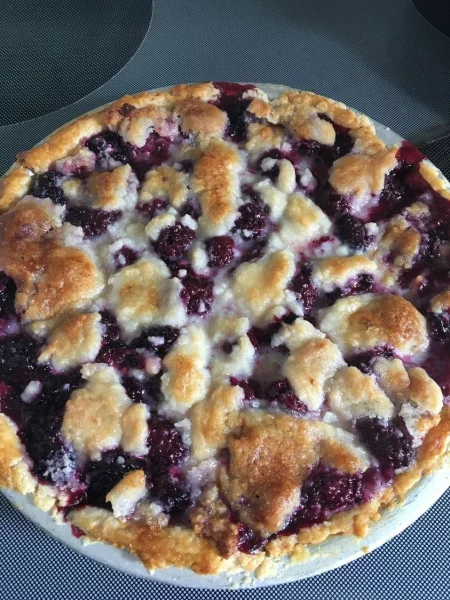 A baked blueberry cobbler in a round baking dish, topped with golden brown crust.