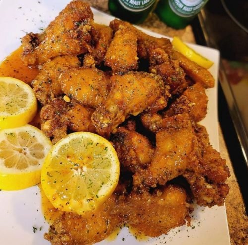 A plate overflowing with golden brown chicken wings glazed in a sticky honey garlic sauce with lemon pepper seasoning.