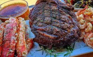 A beautifully plated Tomahawk steak, king crab, shrimp and brussel sprouts on a white plate