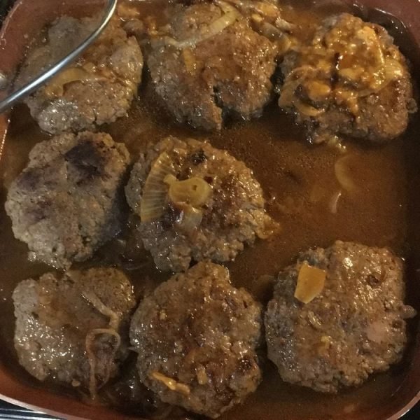 "Hamburger steak with caramelized onion gravy served on a white plate"