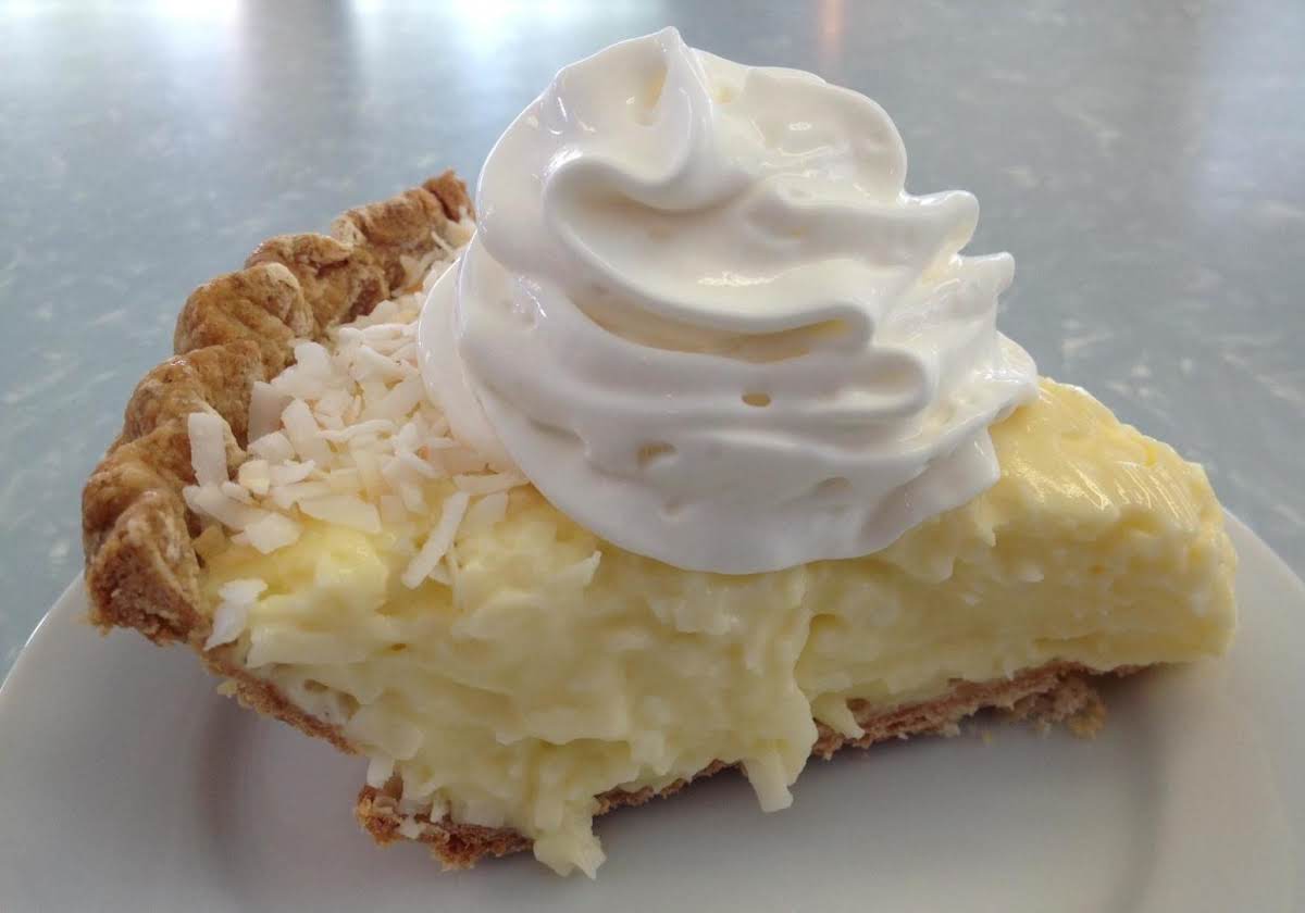 A close-up image of a homemade coconut cream pie on a plate, featuring a golden brown crust, creamy white filling, and fluffy whipped topping garnished with toasted coconut flakes.