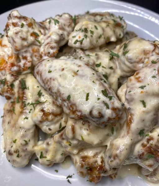 Close-up of creamy Alfredo chicken wings on a white plate.