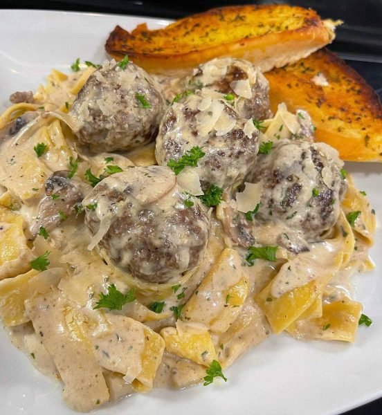 A plate of hot and delicious mushroom and meatball pasta, garnished with Parmesan cheese and fresh parsley