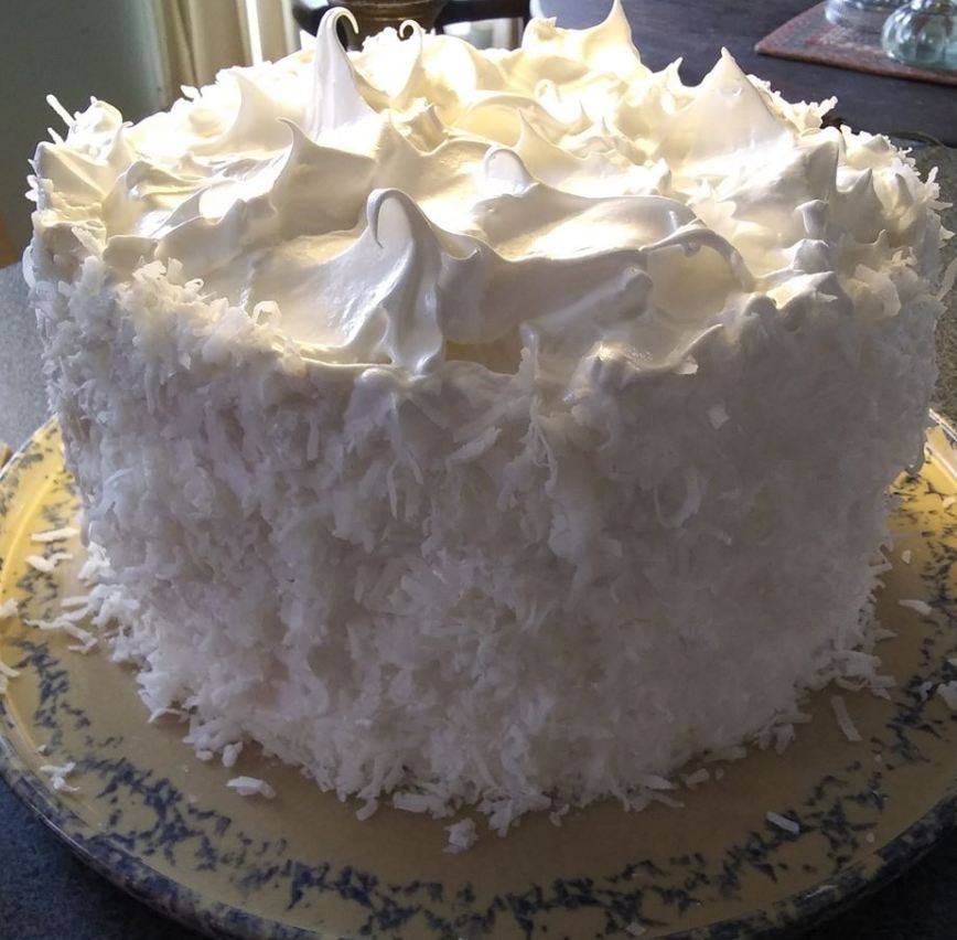 A three-layer Coconut Cake with Seven-minute Frosting on a white plate.
