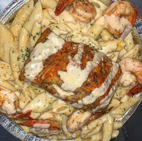 A beautifully plated dish of Crab Stuffed Salmon and Shrimp Alfredo Pasta, garnished with fresh herbs and lemon.