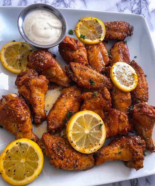 Crispy lemon pepper chicken wings on a white plate garnished with parsley and lemon wedges