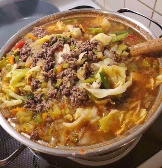 Bowl of delicious and steaming cabbage soup topped with fresh herbs.