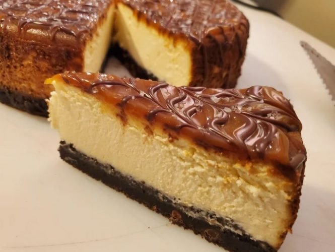 Salted Caramel Brownie Cheesecake on a cake stand, showcasing layers of fudgy brownie, creamy cheesecake, and a drizzle of salted caramel.