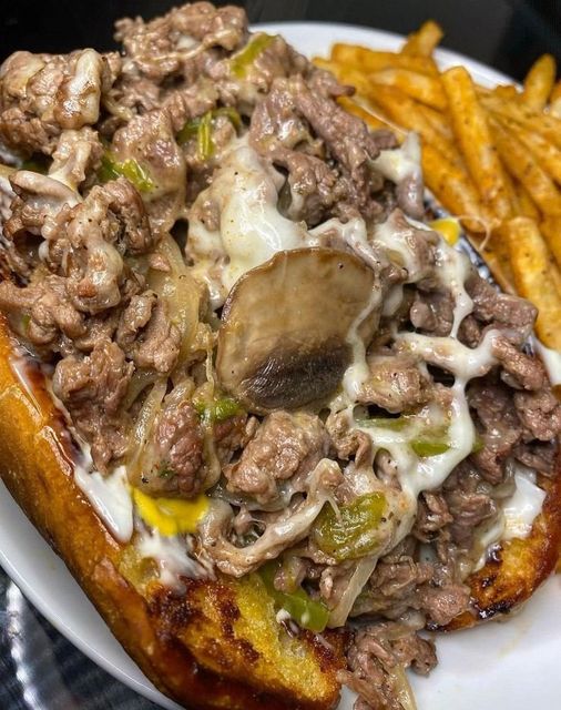 "Image showcasing a perfectly crafted Philly Cheesesteak with prime ribeye, melted cheese, sautéed onions, bell peppers, and flavorful seasonings."