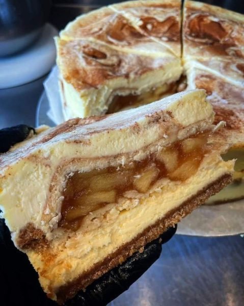 A slice of Apple Pie Stuffed Cheesecake on a plate, with a fork and whipped cream on the side.