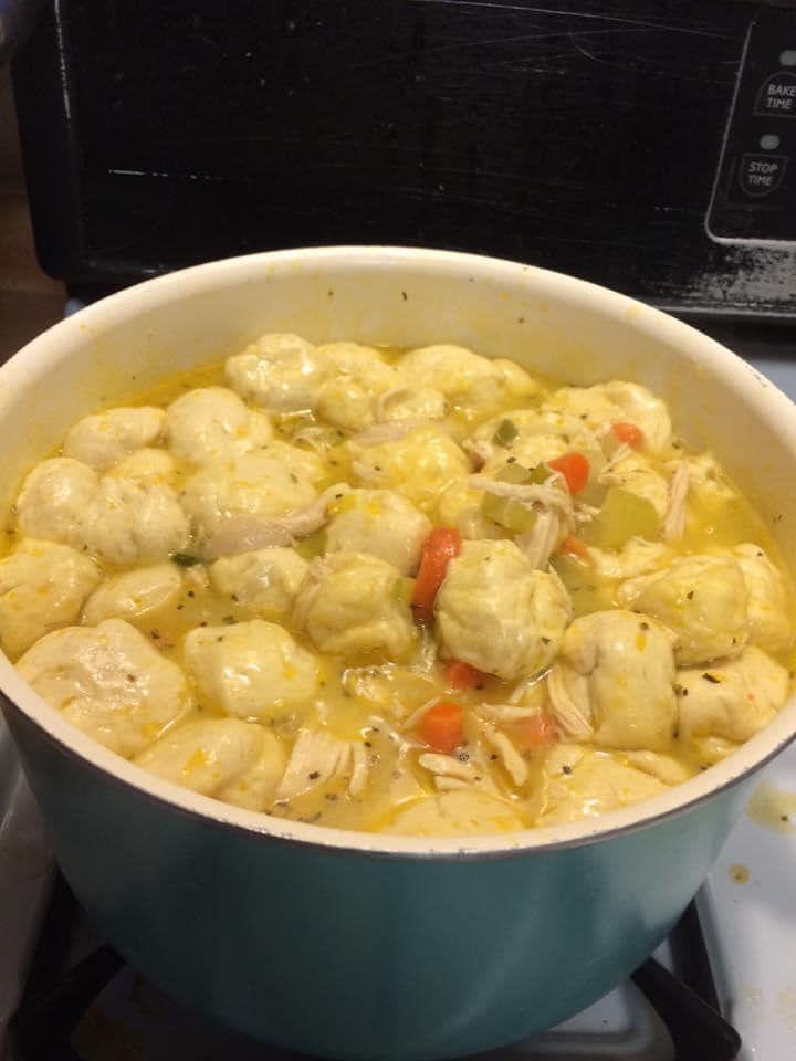 Flattened refrigerated biscuit dough being artfully layered on top of simmering Crock Pot Chicken and Dumplings in a slow cooker.