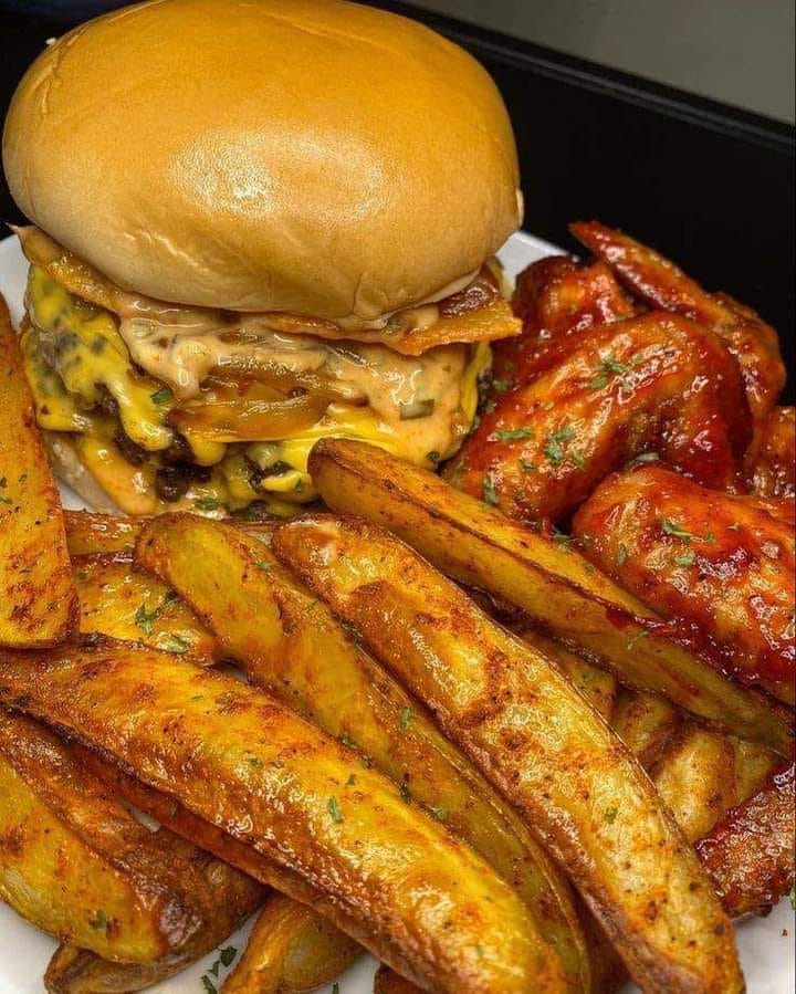 A cheeseburger topped with cheddar cheese, lettuce, tomato, and onion, served with western fries and wings on the side
