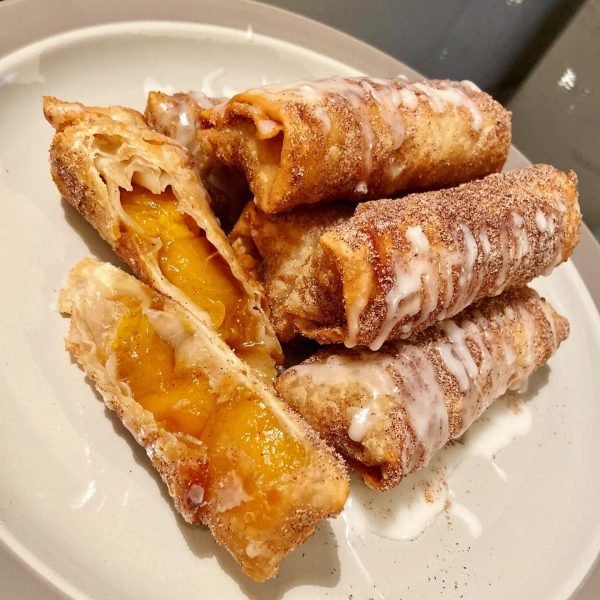 A plate of crispy Peach Cobbler Egg Rolls with a scoop of vanilla ice cream on the side.