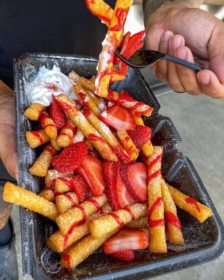 Golden brown strawberry funnel cake fries dusted with powdered sugar and topped with cooked strawberries