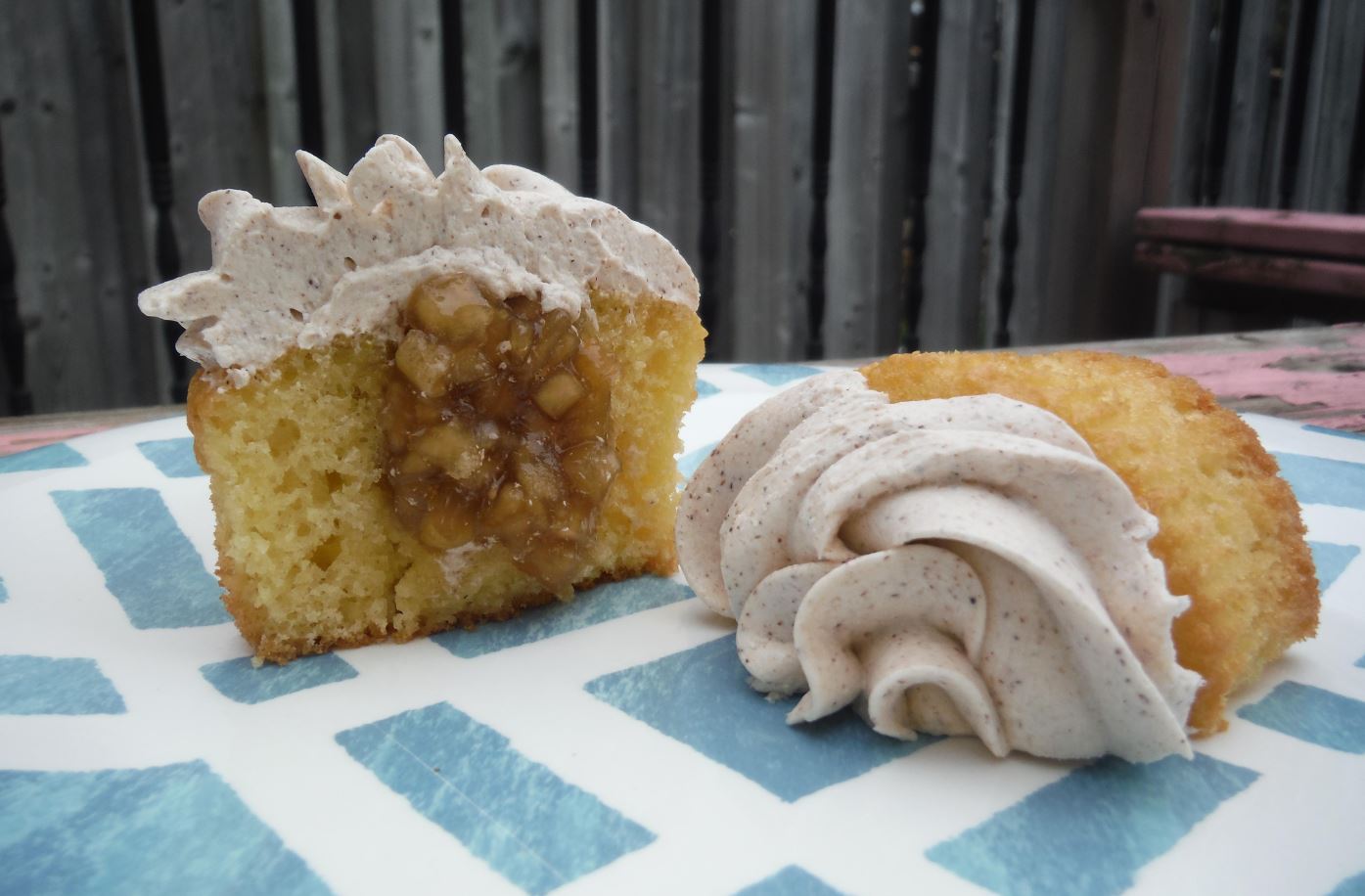 Image of a freshly baked Apple Pie Cupcake with a golden brown cupcake base, a spiced apple filling, and a white swirl of cinnamon buttercream frosting.