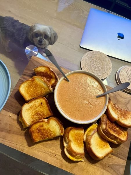 A bowl of creamy roasted tomato soup with basil and a grilled cheese sandwich on the side