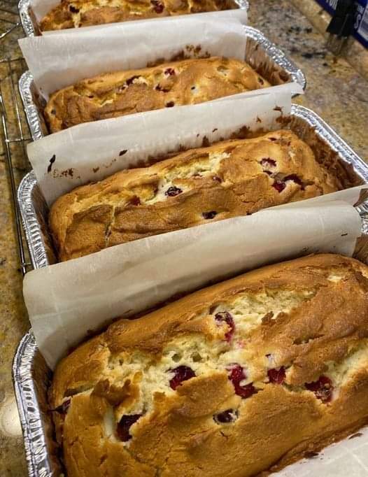 A close-up photo of a sliced Cream Cheese Cranberry Loaf on a plate. The loaf is golden brown on the outside and has swirls of cream cheese and bright red cranberries throughout.