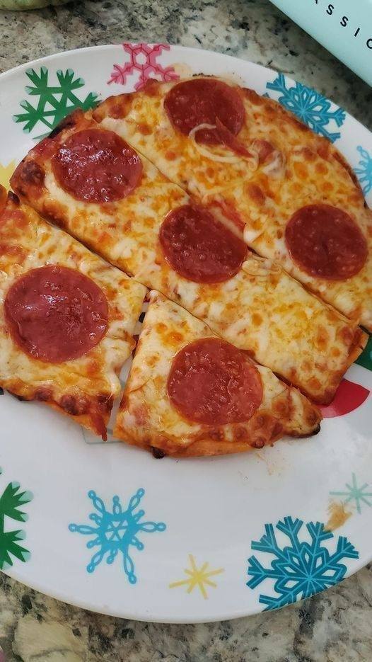 Tortilla pizza topped with fresh vegetables, melted cheese, and savory sauce on a baking sheet