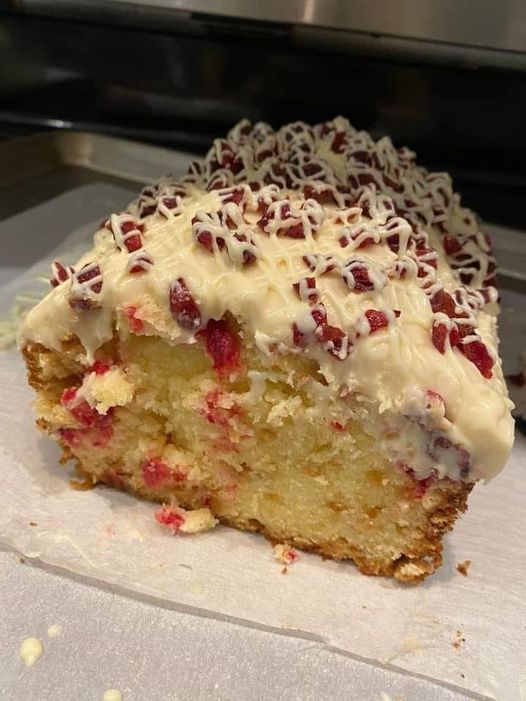 A loaf of Cranberry Orange Bread on a wire rack, drizzled with a white glaze and garnished with fresh cranberries.