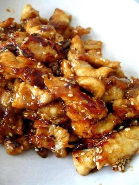 Crock Pot Sesame Chicken - Golden honey, bourbon, and soy sauce-infused chicken bites, sprinkled with sesame seeds, served over rice.