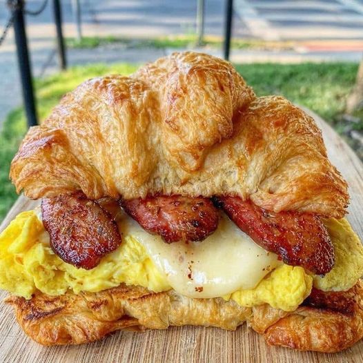 A golden brown croissant cut in half, filled with crispy bacon, fluffy scrambled eggs, and melted cheddar cheese.