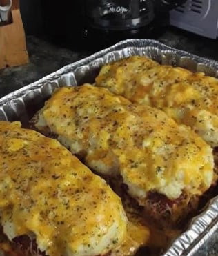 A close-up of a meatloaf on a plate, topped with melted cheese and served with mashed potatoes.