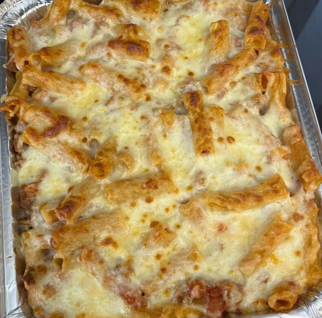 A bubbling hot baking dish filled with rigatoni pasta in a creamy tomato sauce, topped with melted mozzarella cheese and a sprinkling of fresh parsley.