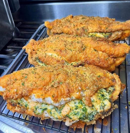 A golden brown baked catfish with a creamy cheese, spinach, and shrimp stuffing visible through the top.