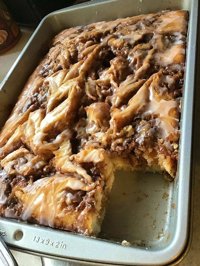 A close-up photo of a sliced Cinnabon Cinnamon Roll Cake revealing a gooey cinnamon swirl center and a creamy white glaze drizzled on top.