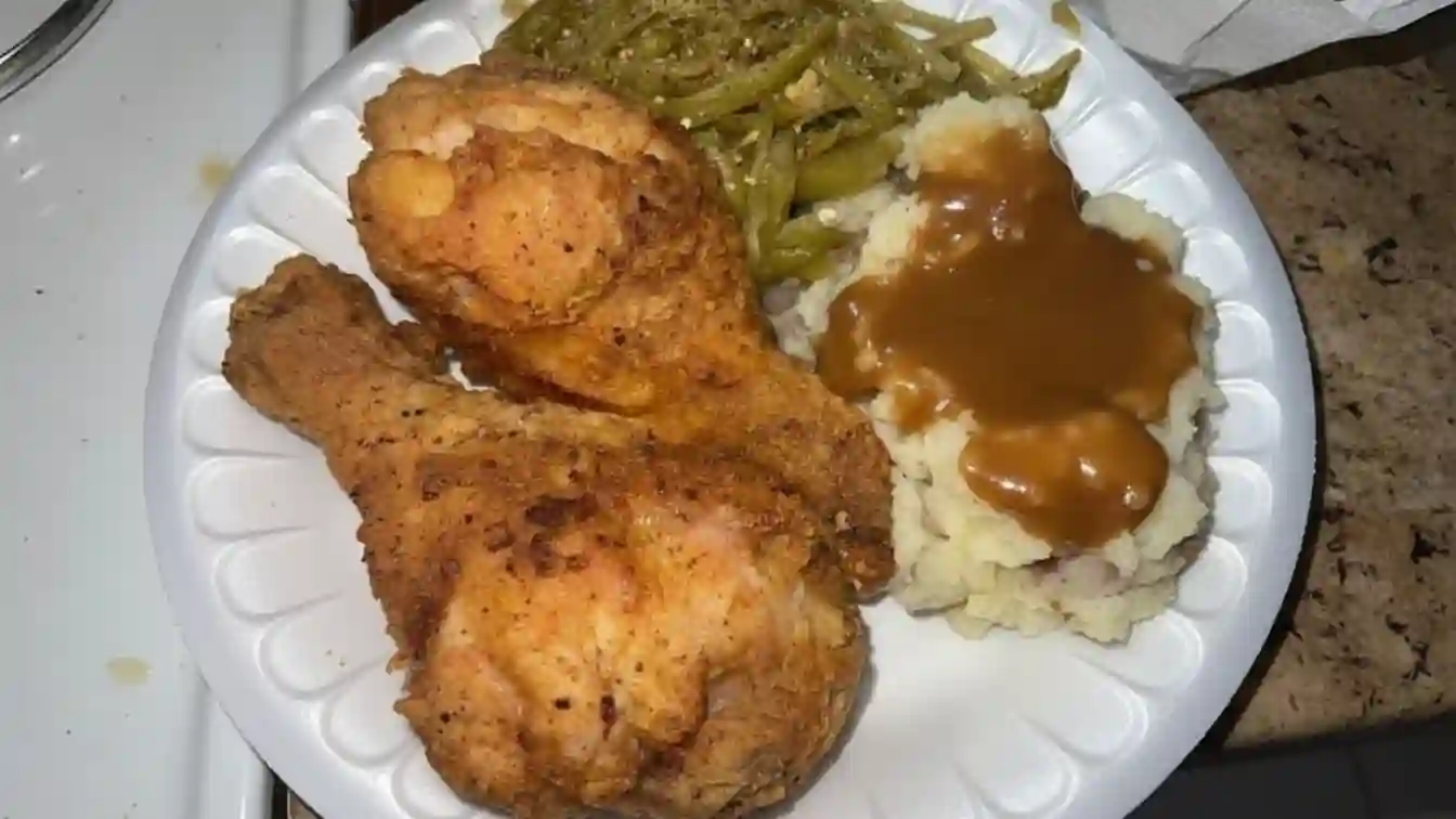 A golden-fried chicken piece served with creamy mashed potatoes on a white plate, a culinary masterpiece of crispy perfection."