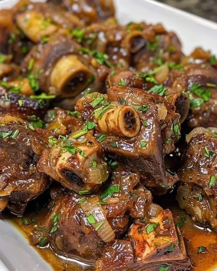 A hearty plate of braised oxtails garnished with fresh herbs and served with mashed potatoes.