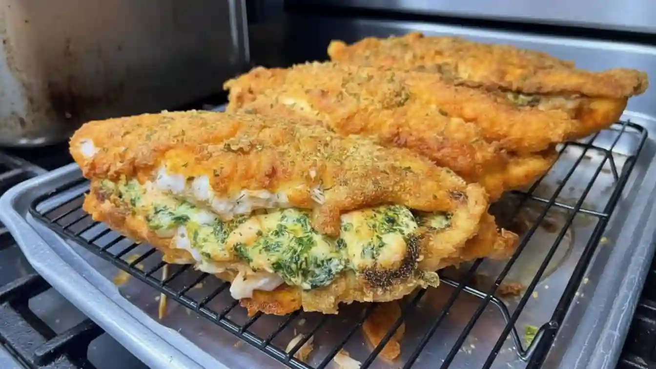 A golden brown baked catfish with a creamy cheese, spinach, and shrimp stuffing visible through the top.